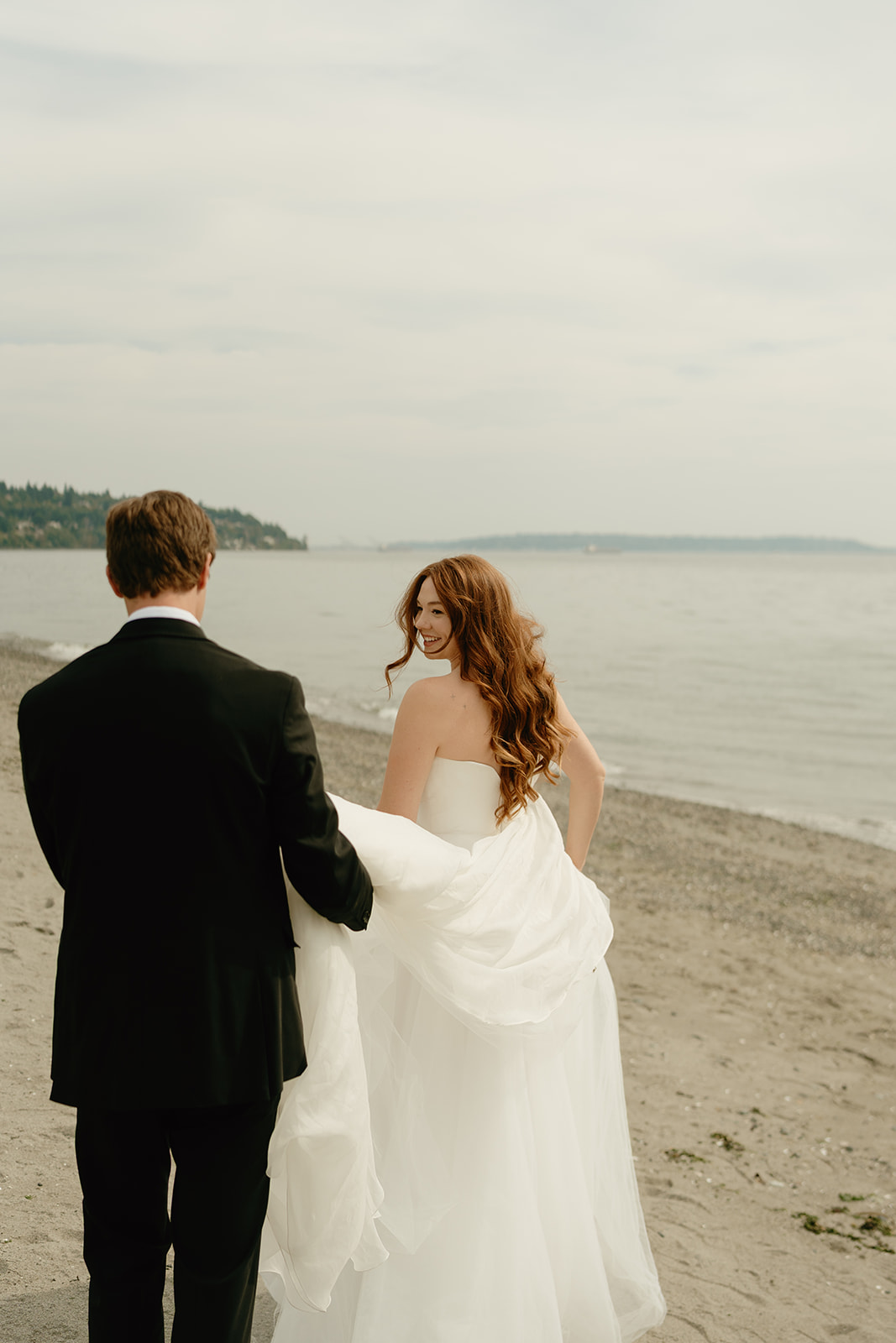 Bride and groom walking along the shoreline, waves gently meeting the sand during a peaceful wedding in Washington.