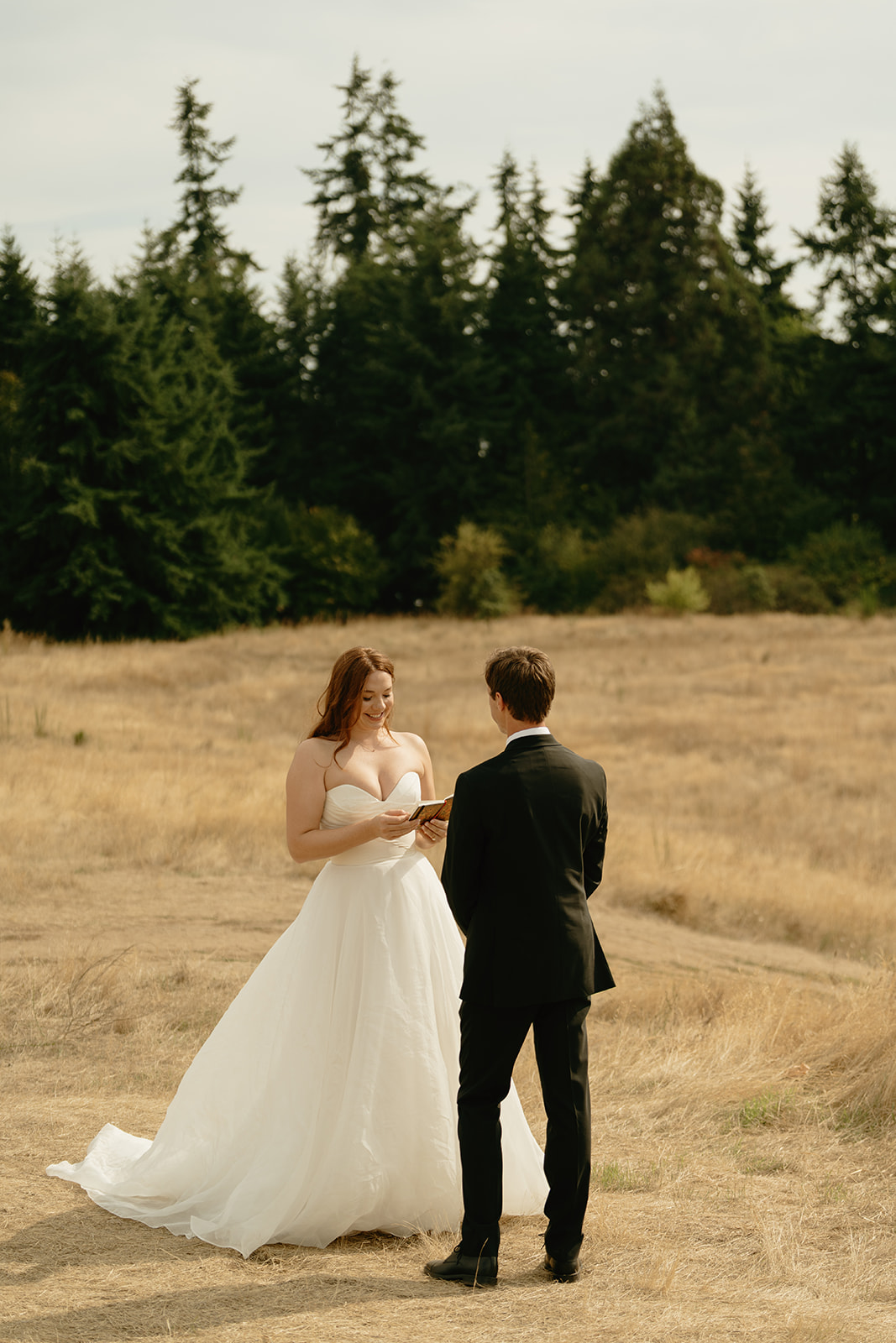 Bride reading her vows in an open field surrounded by tall grasses and evergreens during an outdoor wedding in Washington.