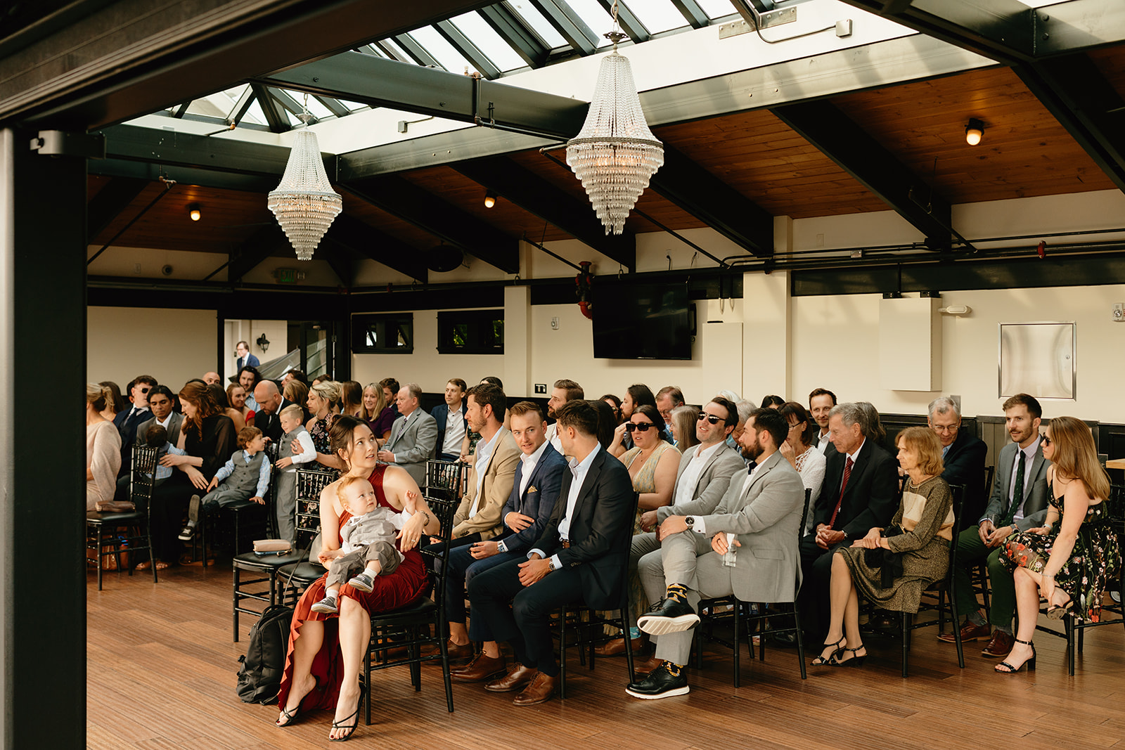 Guests gather beneath chandeliers at a modern indoor venue, waiting for the ceremony to begin.