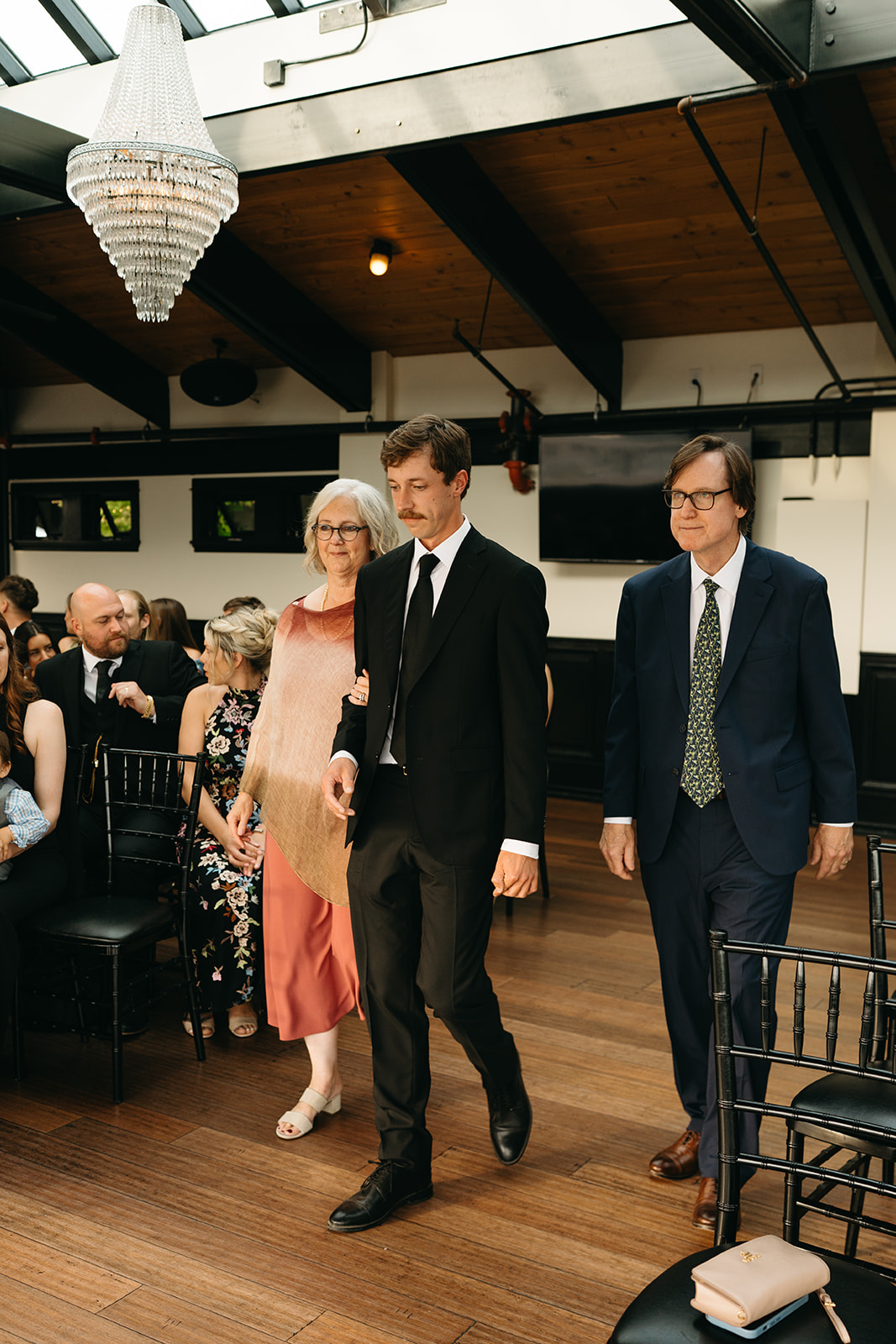 Groom walking down the aisle arm-in-arm with his parents before the ceremony begins.