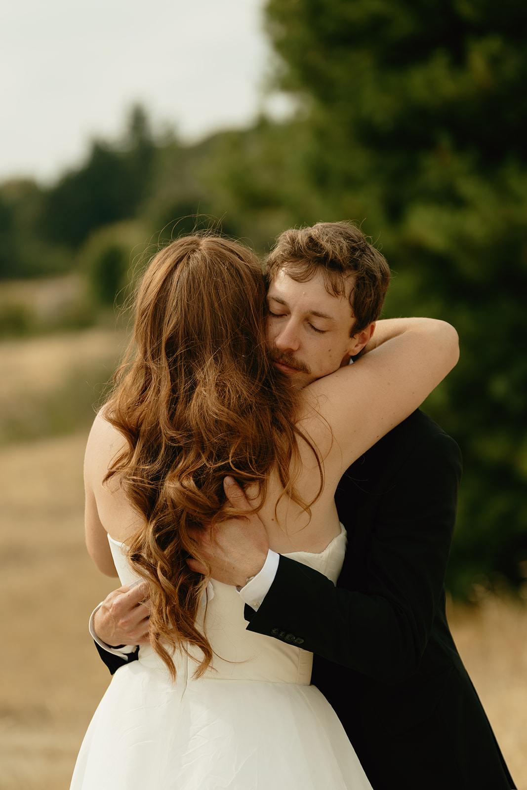 Emotional embrace between the bride and groom in a quiet field, surrounded by soft golden light.