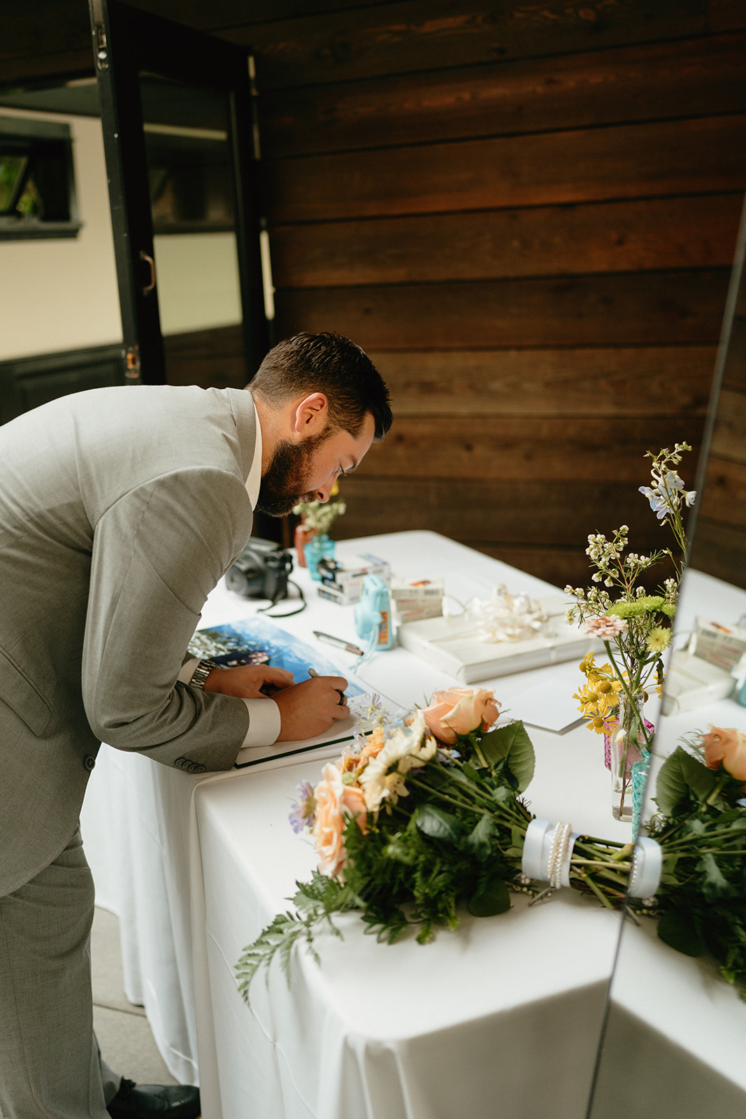 Guest writing a message beside a soft floral arrangement at a Washington wedding reception welcome table.