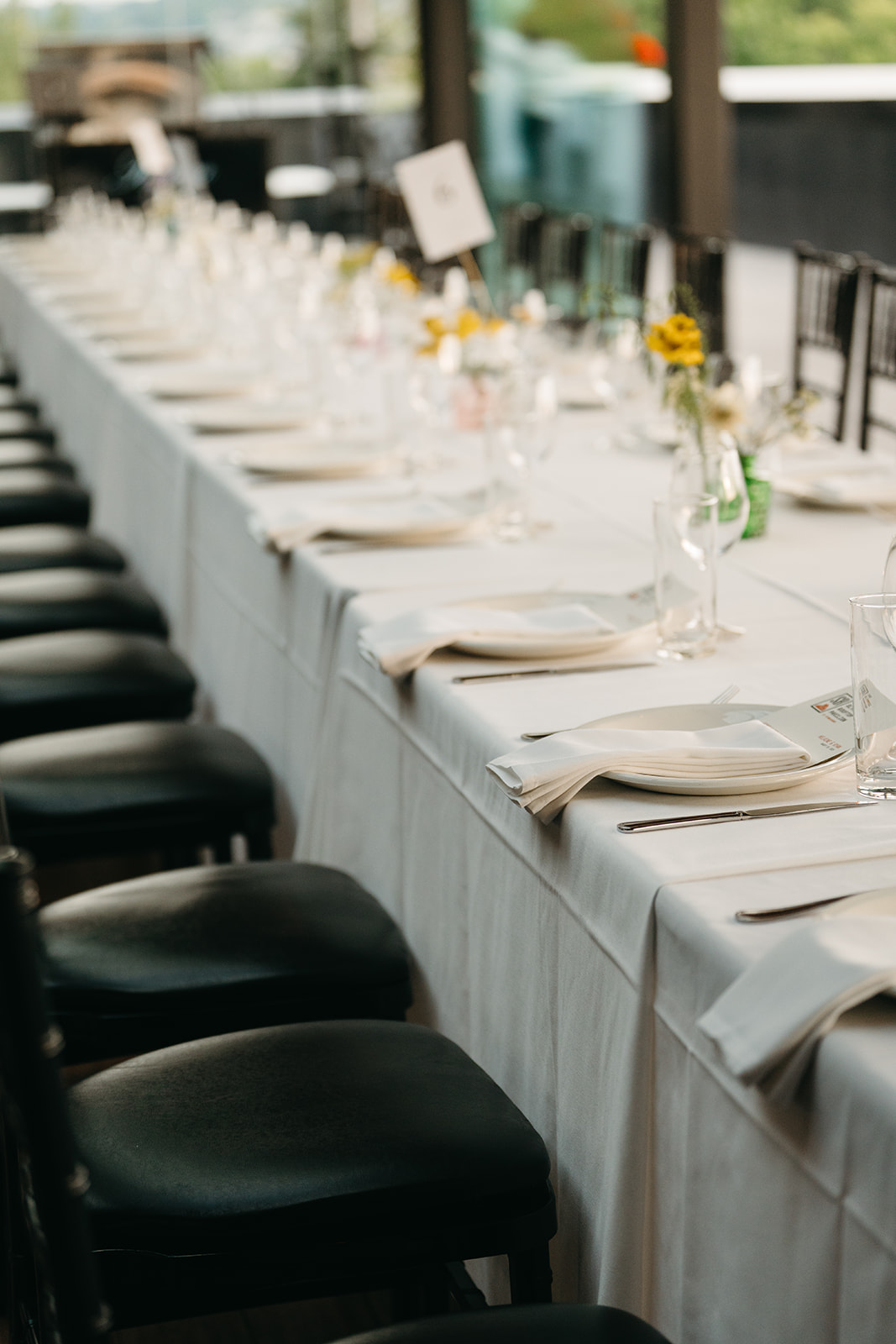 Reception table set for a wedding in Washington, with soft white linens, classic black chairs, and wildflower bud vases lining the center.