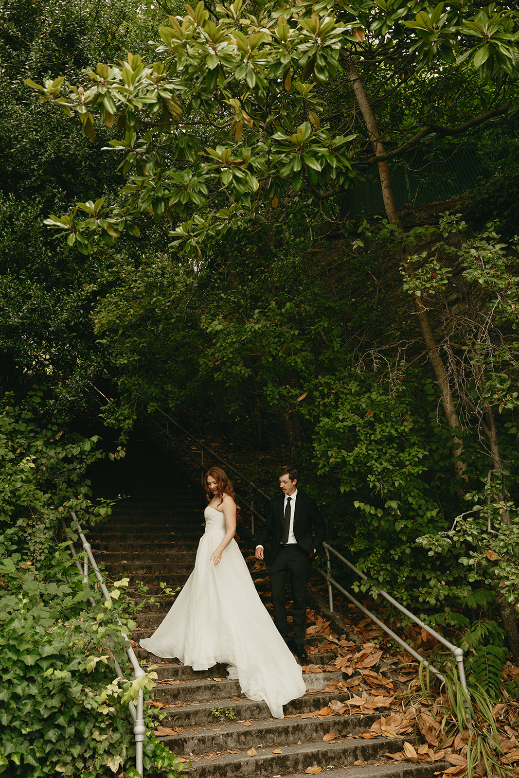 Bride and groom walk down moss-covered stone steps beneath a canopy of green during their wedding in Washington.