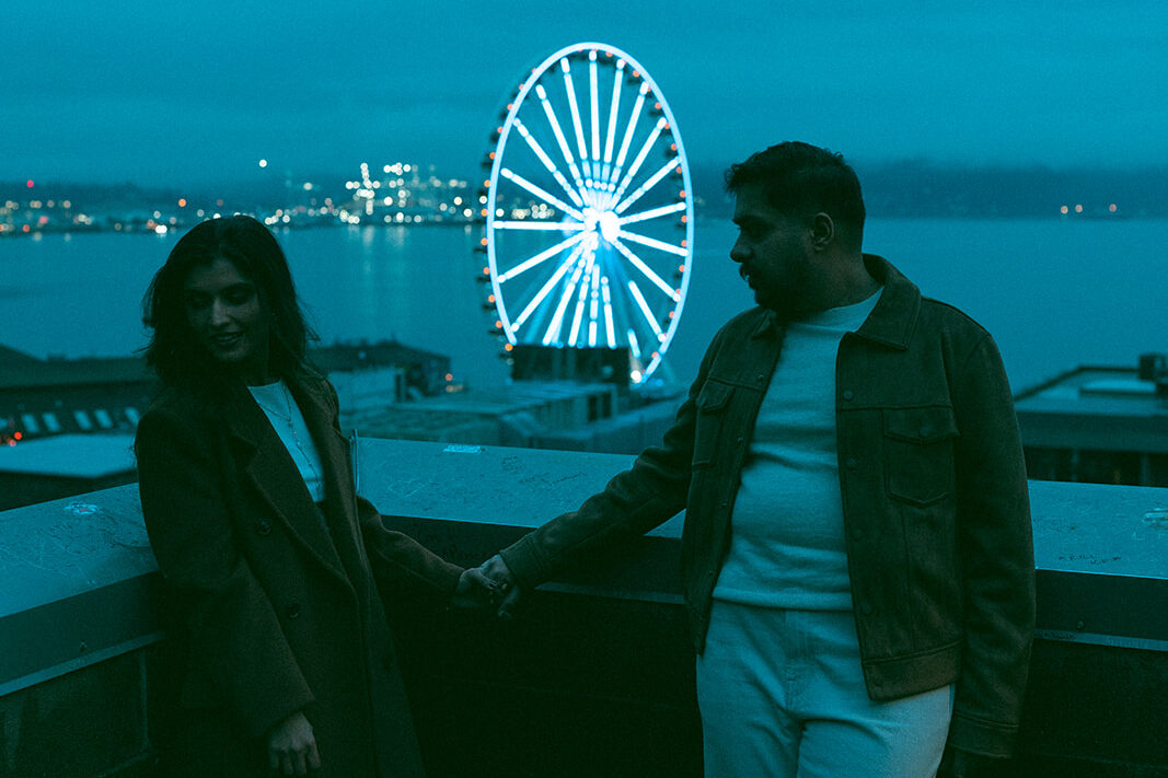 A cinematic couple holding hands in front of the Seattle ferris wheel