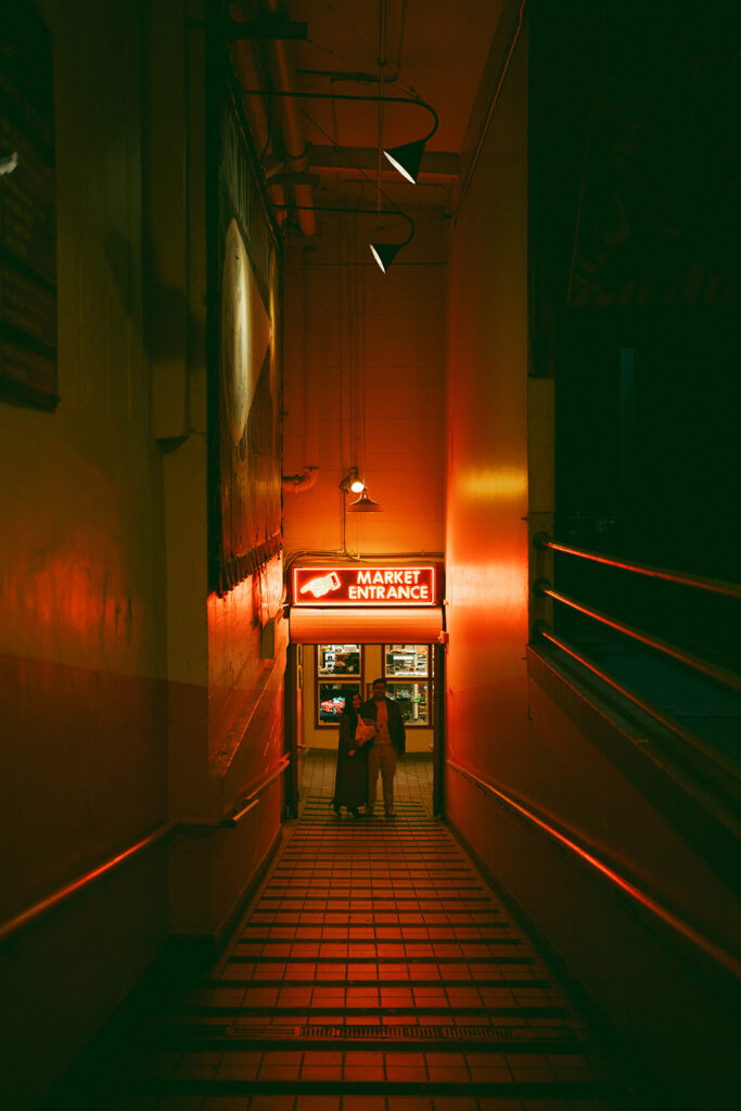 Wide cinematic image of couple under a red glowing market entrance sign in Seattle