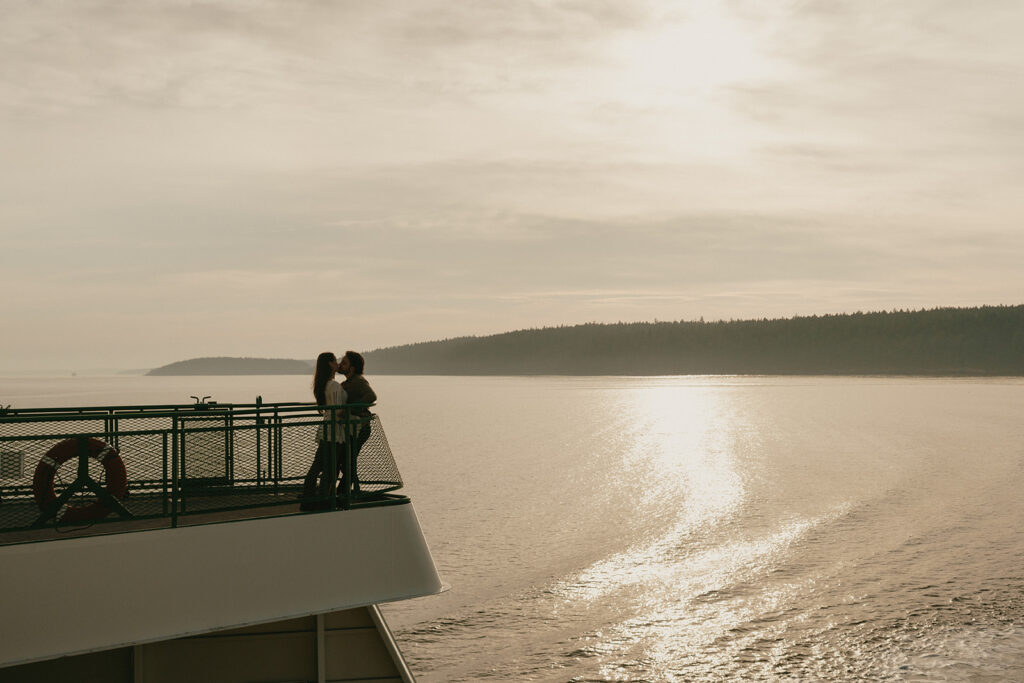 A couple standing on a Washington State ferry during golden hour, overlooking the glowy water of the San Juan Islands.